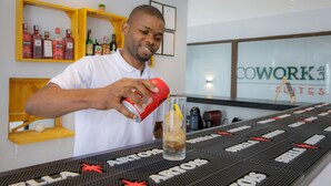 A bartender pouring a drink into a glass at a bar with a black mat displaying the word "COWORK" and "SUITES". - Cowork Lab Suites (Maputo)