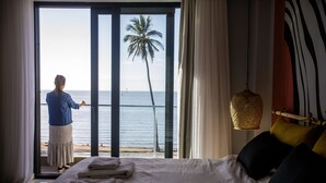 Habitación de hotel con una cama, vista al mar y una persona de pie junto a la ventana.