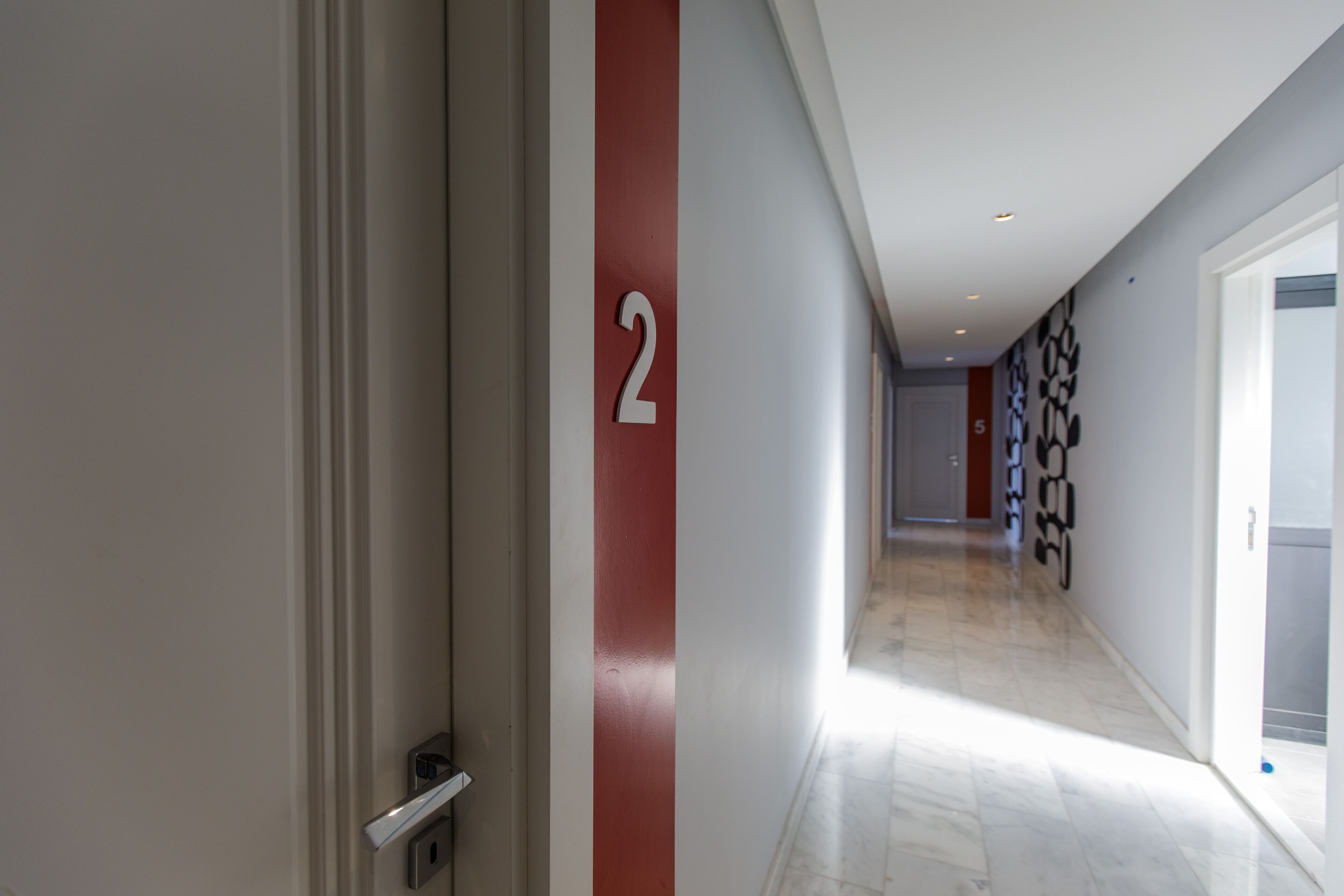 Un couloir avec une porte et un mur orné de motifs, et un panneau indiquant le numéro « 2 ».