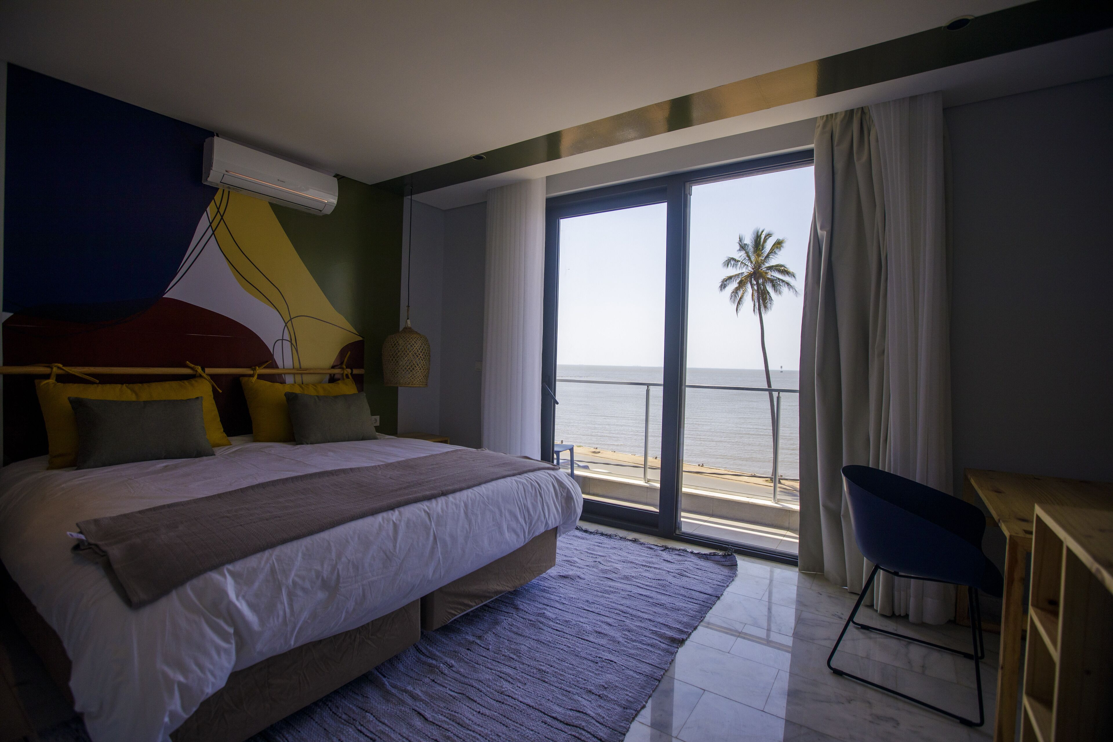 A bedroom with a large bed, a desk, and a view of the sea.