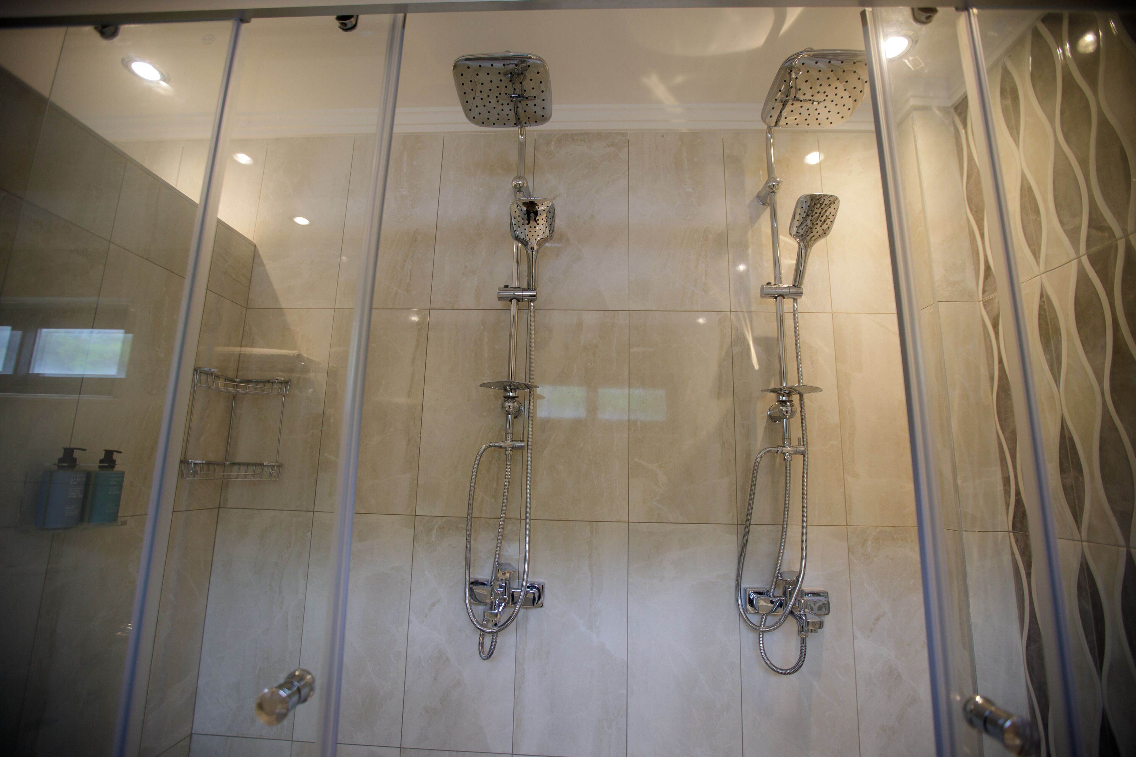 A glass-enclosed shower area with two showerheads and a handheld showerhead.