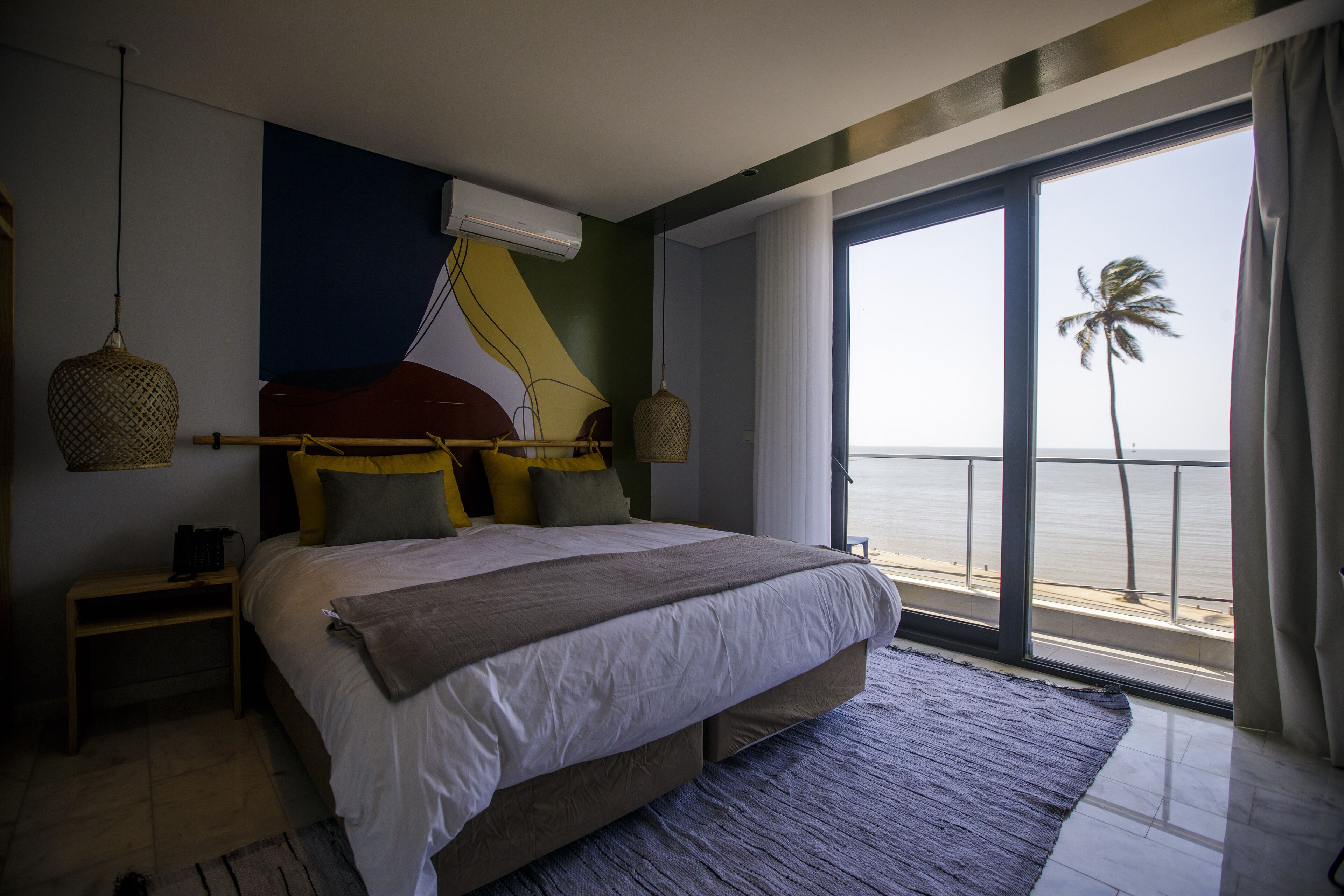 Une chambre avec un grand lit, une vue sur la mer et un balcon agrémenté d’un palmier.