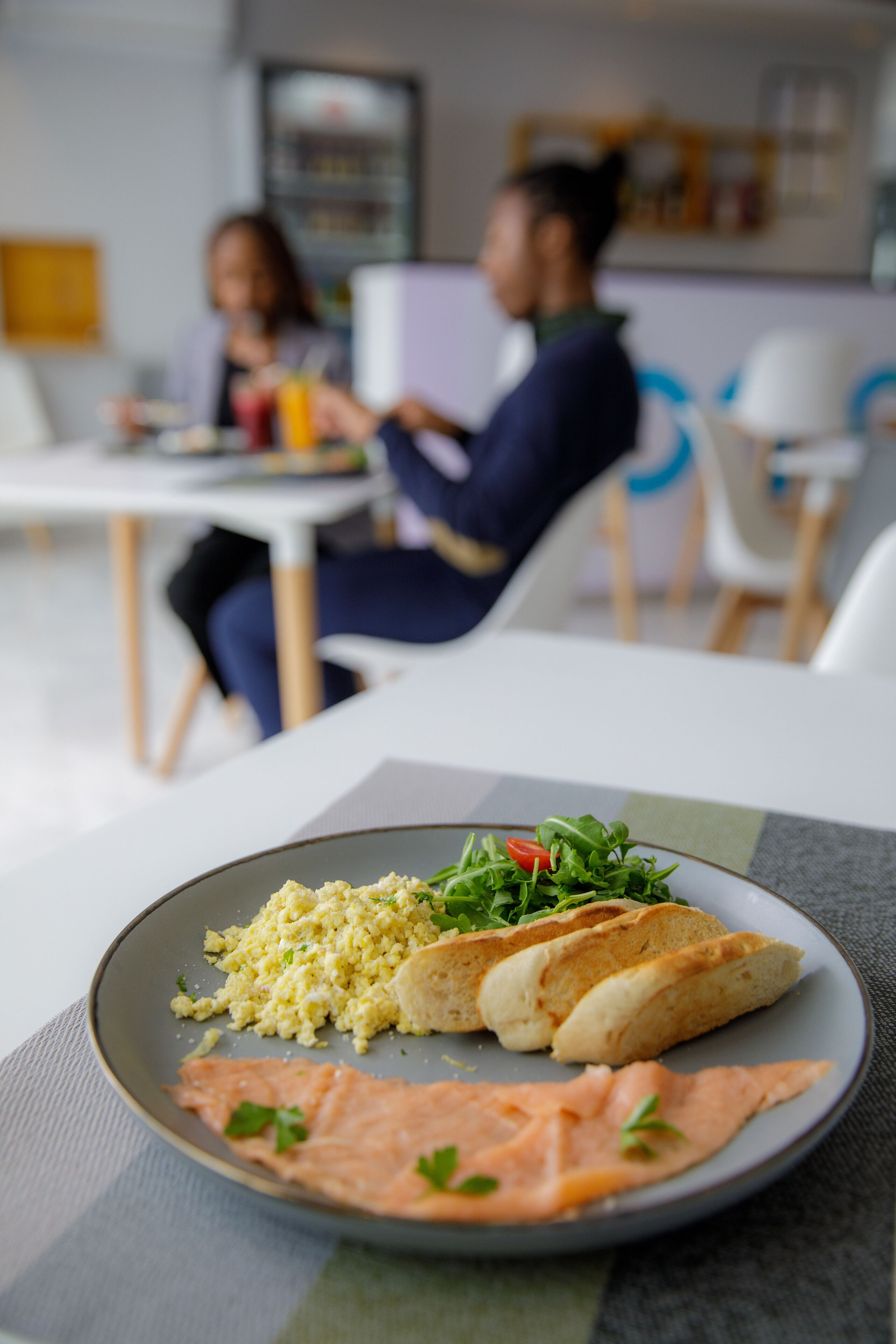 Un piatto con salmone e verdure su un tavolo in una sala da pranzo moderna, con sedie e tavolo bianco.