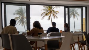 A group of people seated at a table with a view of palm trees through large windows. - Cowork Lab Suites (Maputo)