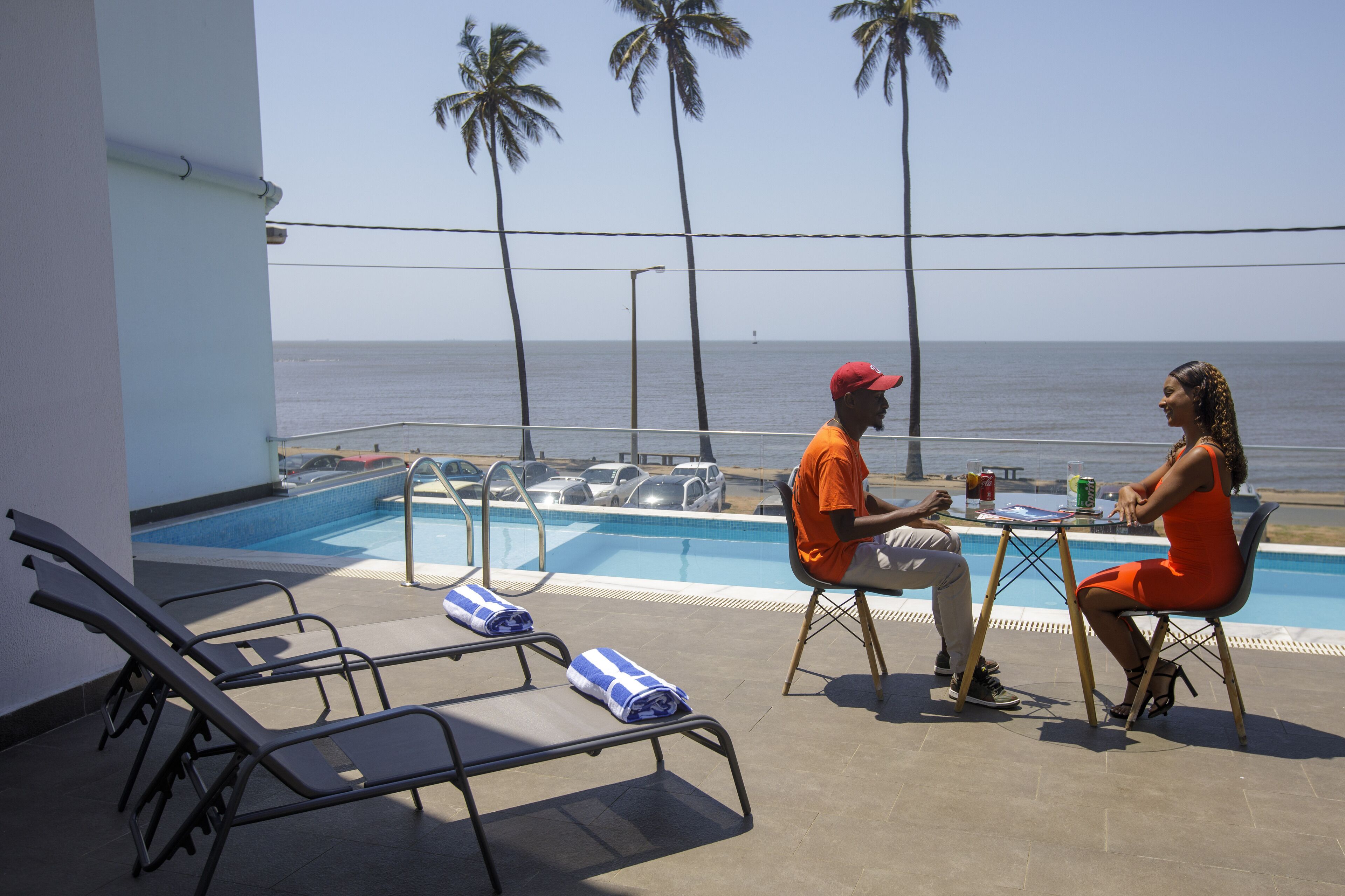 Zona junto a la piscina con sillones de descanso, una mesa y vista al océano.
