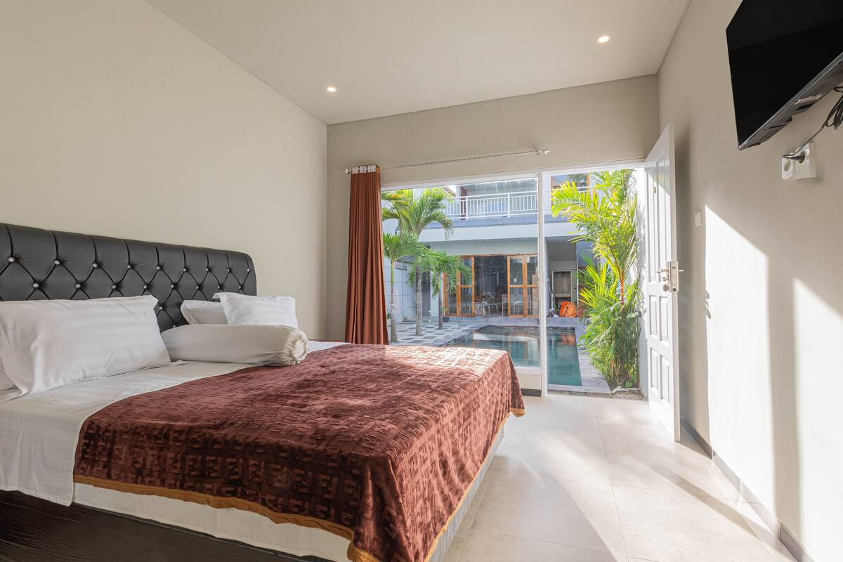 A modern bedroom with a large bed, a tufted headboard, and a view of a pool and outdoor area.