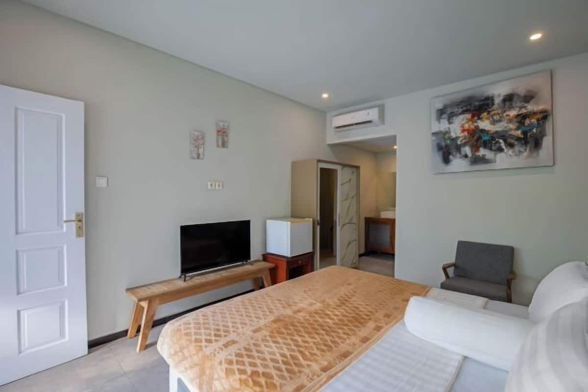 A hotel room with a bed, a TV, a chair, and a painting on the wall.