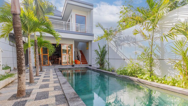 Una casa moderna de dos pisos con piscina, palmeras y un piso con estampado de cuadros.