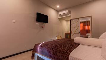 A hotel room with a bed, a television mounted on the wall, an air conditioning unit, and a door leading to a bathroom.