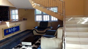 A hotel lobby with a reception desk, a staircase, and two leather chairs. - Westbro hotel and suites  (Lekki)