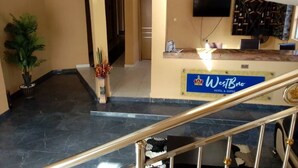 A hotel reception area with a reception desk, a mounted television, and a staircase with a golden handrail. - Westbro hotel and suites  (Lekki)