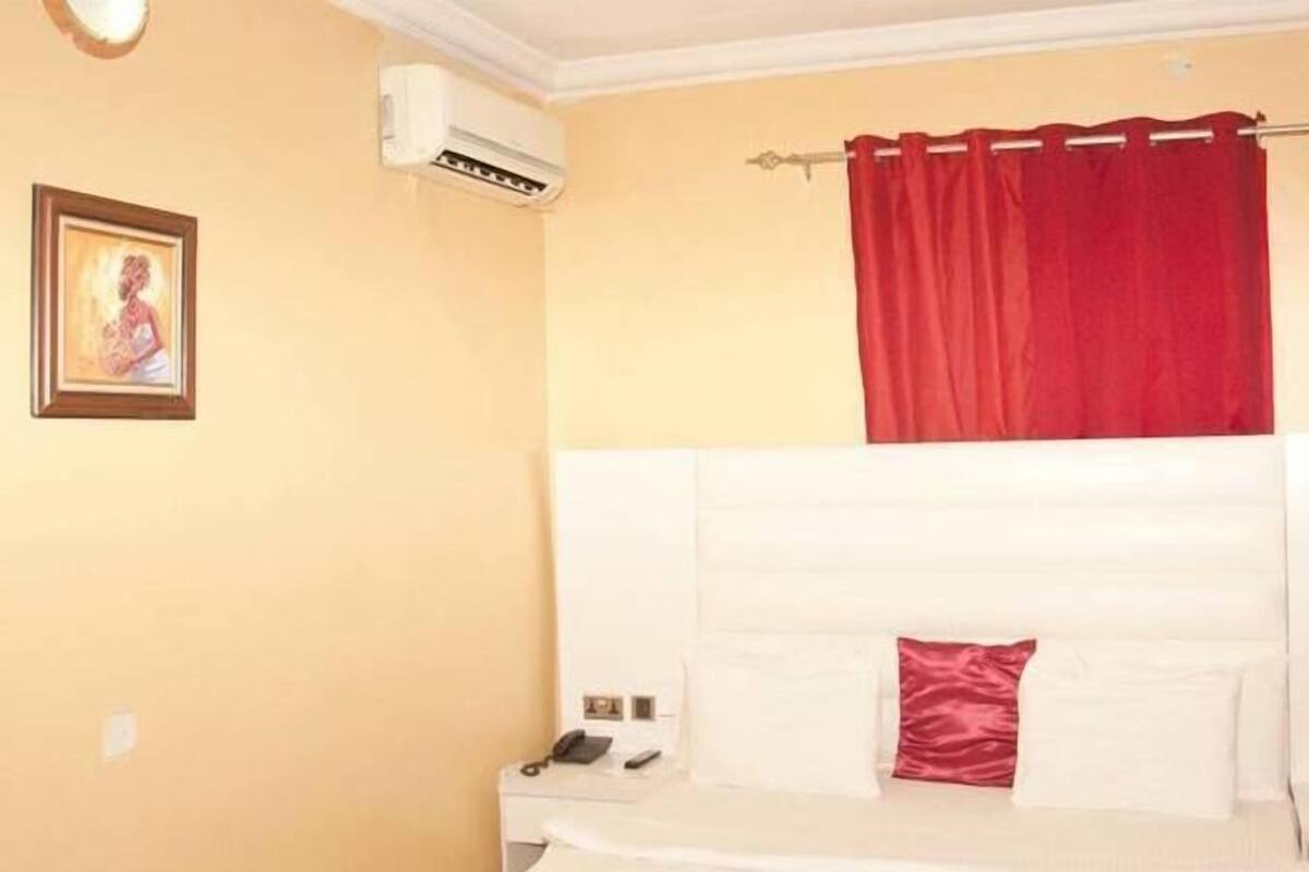 A hotel room with a bed, a nightstand, a telephone, and a wall-mounted air conditioner.