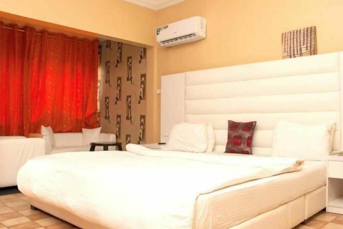 A hotel room with a large bed, a bedside table, a wardrobe, and an air conditioning unit on the wall.