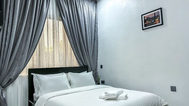 A neatly made bed with white linens, a dark headboard, and a framed picture on the wall. - Westbro hotel and suites  (Lekki)
