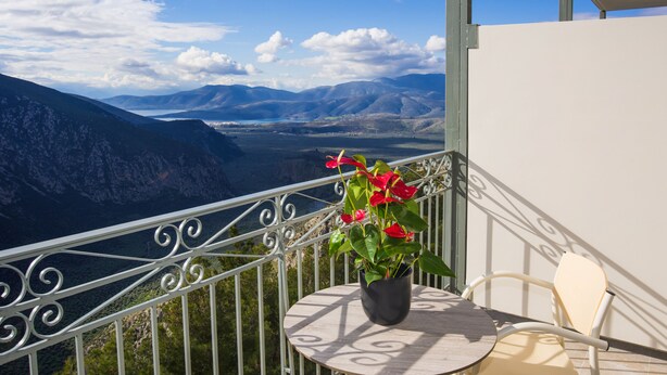 Un balcón con planta en maceta, una mesa y una silla con vista a un paisaje montañoso.