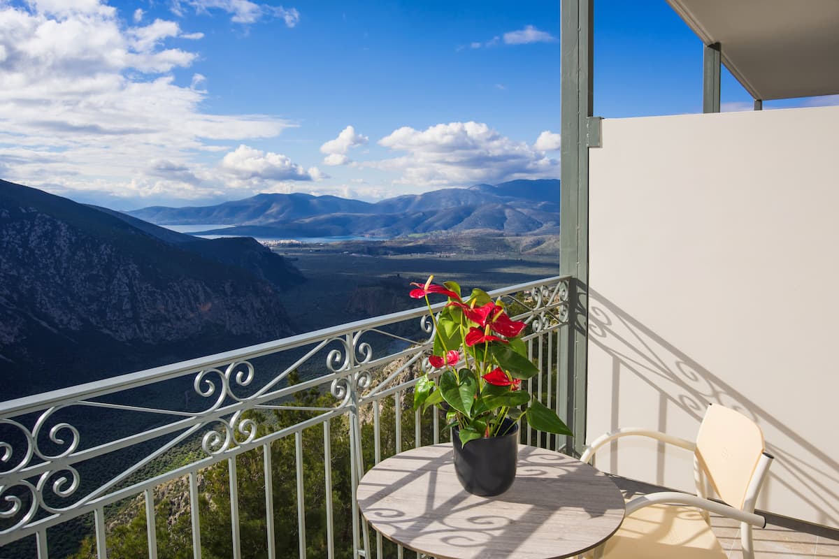 A balcony with a potted plant, a table, and a chair overlooking a mountainous landscape.