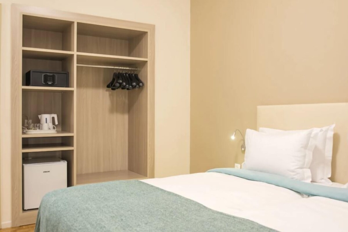 A bedroom with a bed, a nightstand, a closet with shelves, and a small refrigerator.