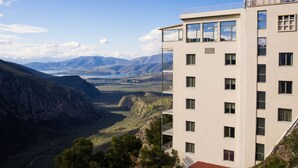 Un hotel de varios pisos con balcones, vista a un paisaje montañoso y banderas en el tejado.