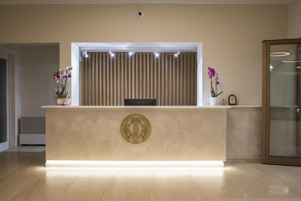 A reception desk with a modern design, featuring a logo in the center, two potted orchids, and a vertical light strip. - V Hotel Delphi (Delphi)