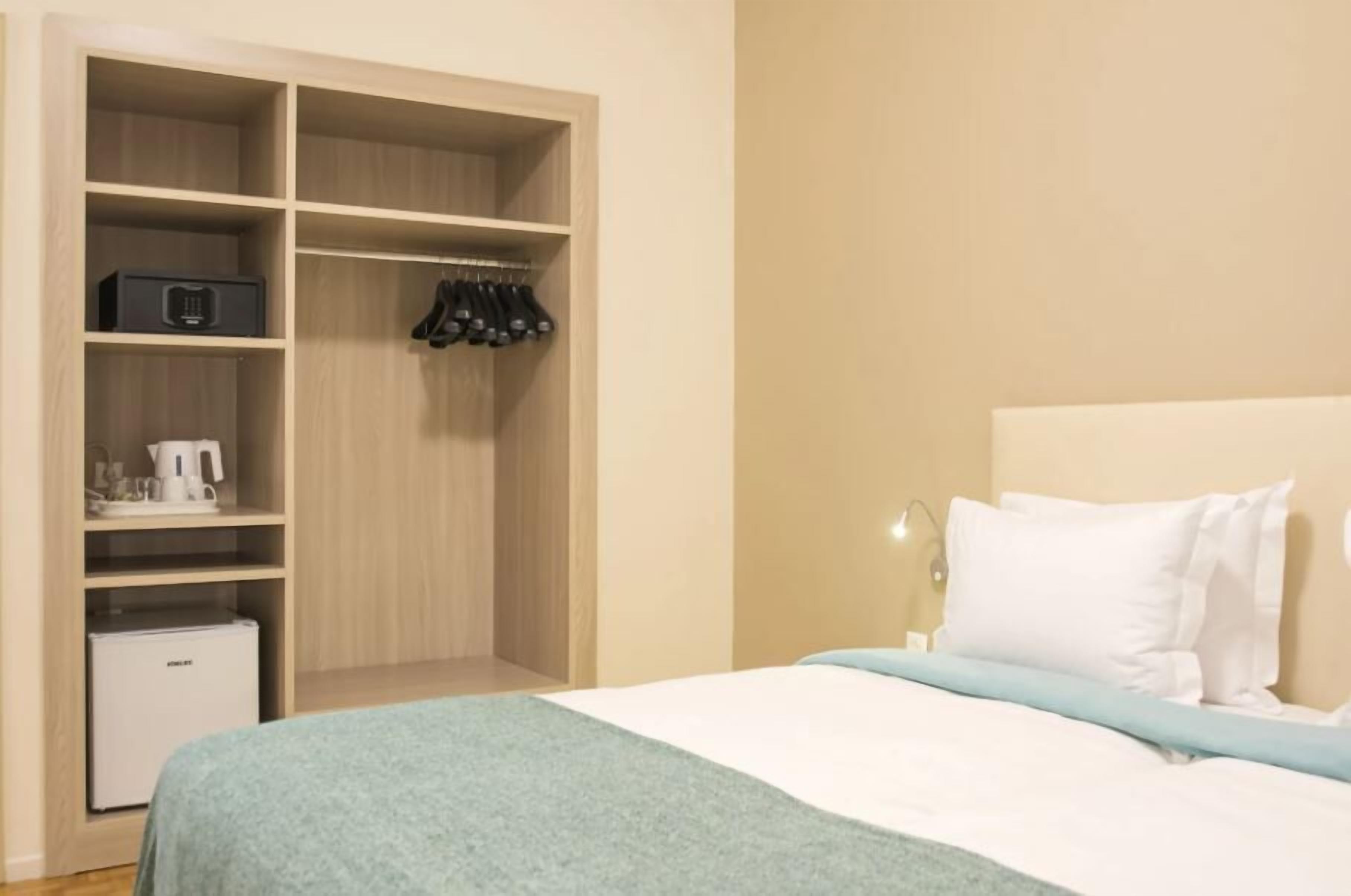 A bedroom with a bed, a nightstand, a closet with shelves, and a small refrigerator.