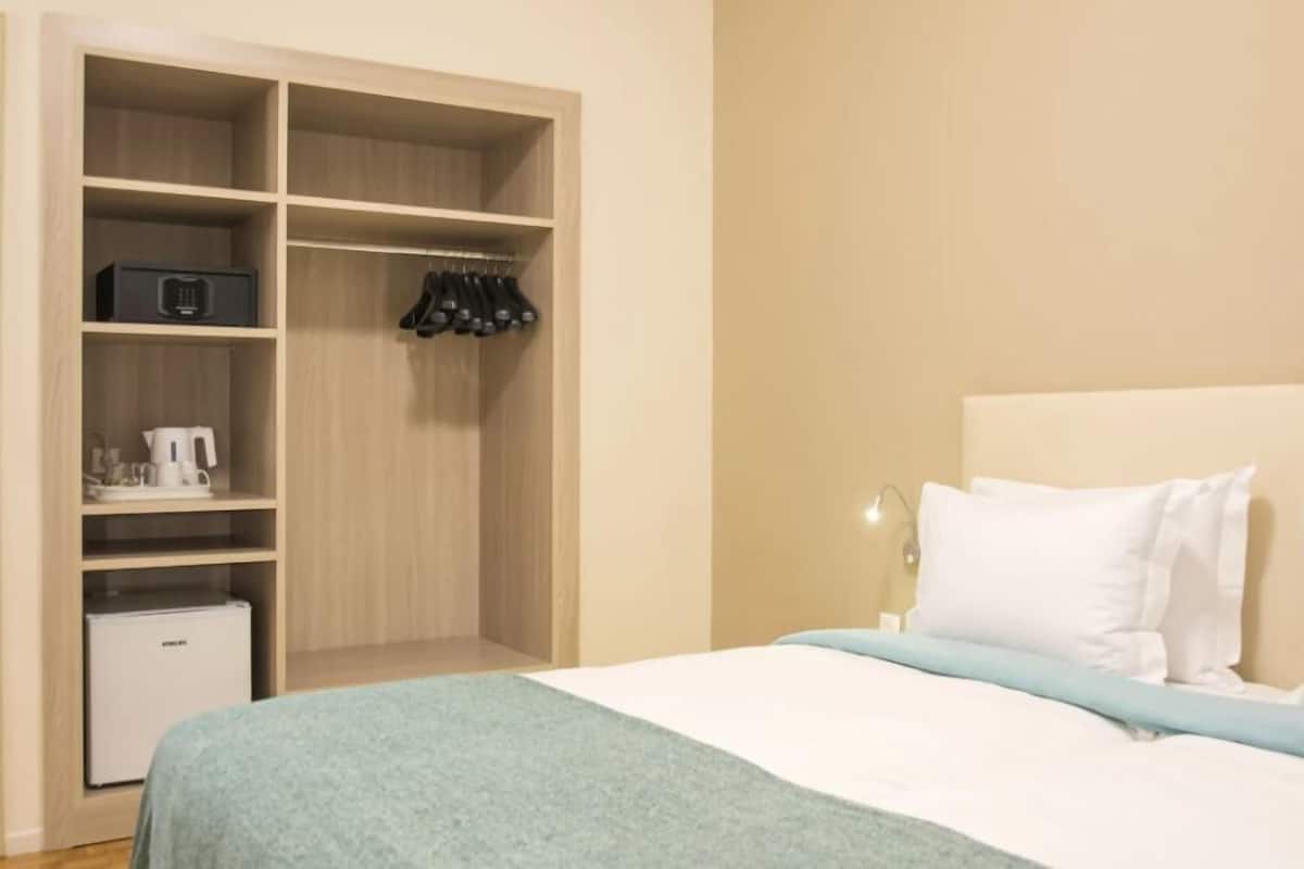 A bedroom with a bed, a nightstand, a closet with shelves, and a small refrigerator.