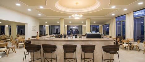 A spacious hotel lobby with a central bar area, multiple seating options, and large windows offering views.