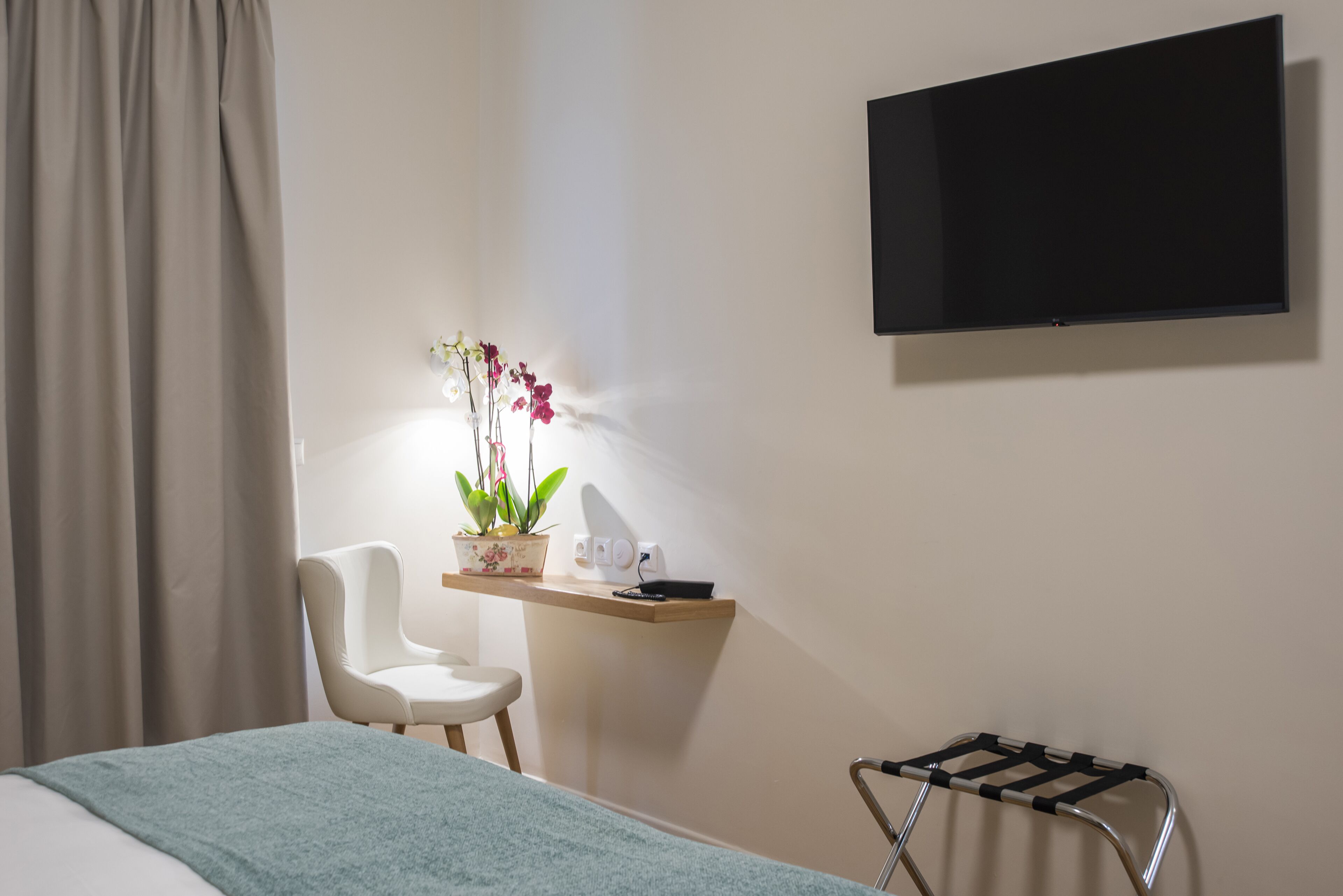 Ein Hotelzimmer mit einem Bett, einem Schreibtisch mit Topfpflanze, einem Sessel, einem Fernseher und einem Handtuchhalter.
