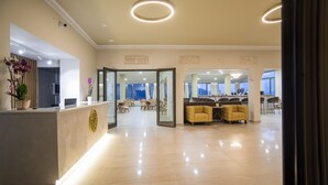 Un moderno vestíbulo de hotel con mostrador de recepción, zona de estar y puertas de vidrio que dan a un comedor.