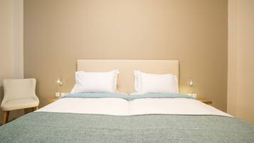 Un lit bien fait, avec du linge de lit blanc et une couverture bleu clair, une chaise blanche et une table de chevet avec une lampe.
