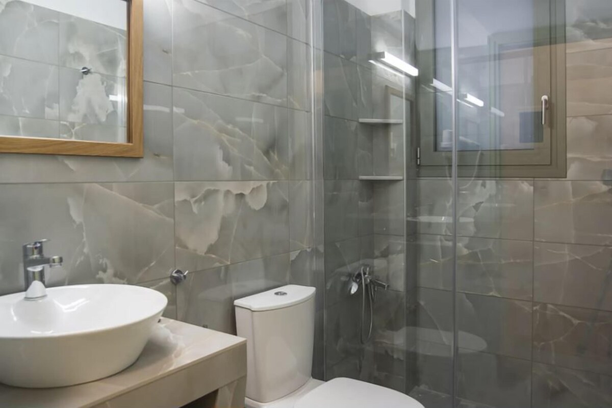 A bathroom with a marble sink, toilet, and glass shower enclosure.