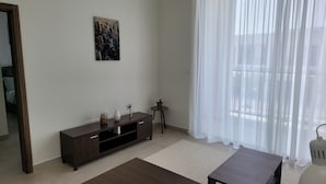 A living room with a dark wooden cabinet, a small round table with a vase, a white rug, and a large window with sheer curtains. - Villa Elena Hayat Island Marbella (Ras Al Khaimah)
