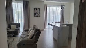 A living room with a sofa, a dining area with a table and chairs, and a painting on the wall. - Villa Elena Hayat Island Marbella (Ras Al Khaimah)