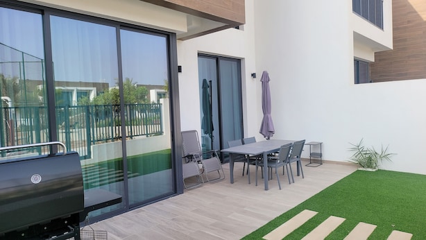 A modern outdoor patio with a dining table and chairs, a grill, and a small garden area with artificial grass. - Villa Elena Hayat Island Marbella (Ras Al Khaimah)