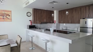 A modern kitchen with wooden cabinets, a stainless steel refrigerator, a microwave, and a sink. There is a clock on the wall and a fire extinguisher on the counter. - Villa Elena Hayat Island Marbella (Ras Al Khaimah)