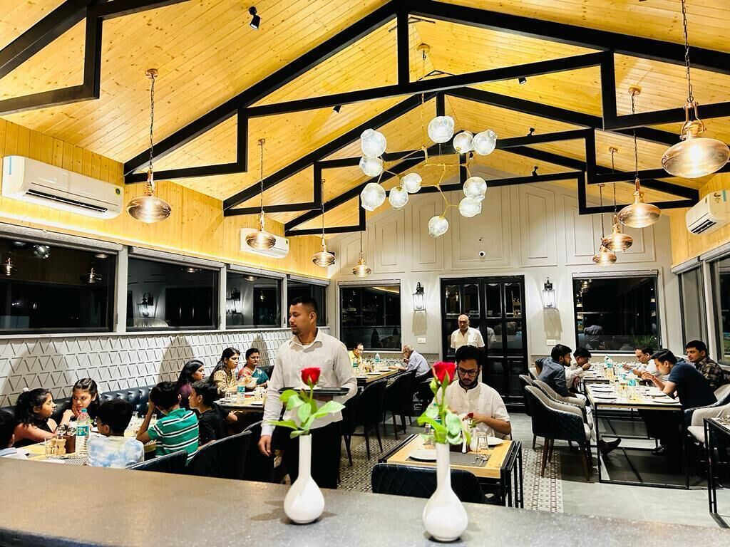 A restaurant with wooden beams and hanging light fixtures. Tables are set with white tablecloths and vases with flowers.