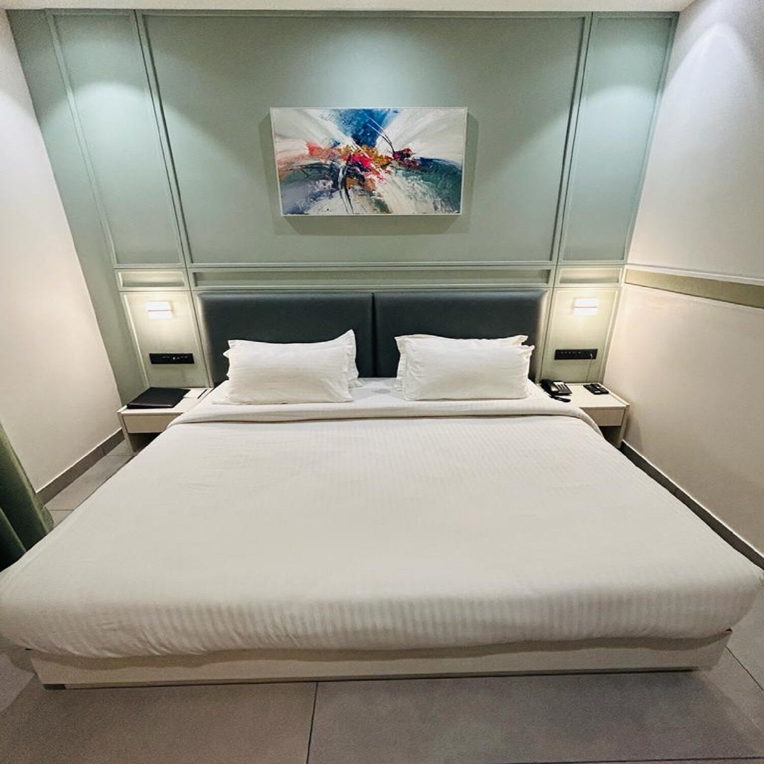 A neatly made bed with white linens, a dark headboard, and two bedside tables with lamps.