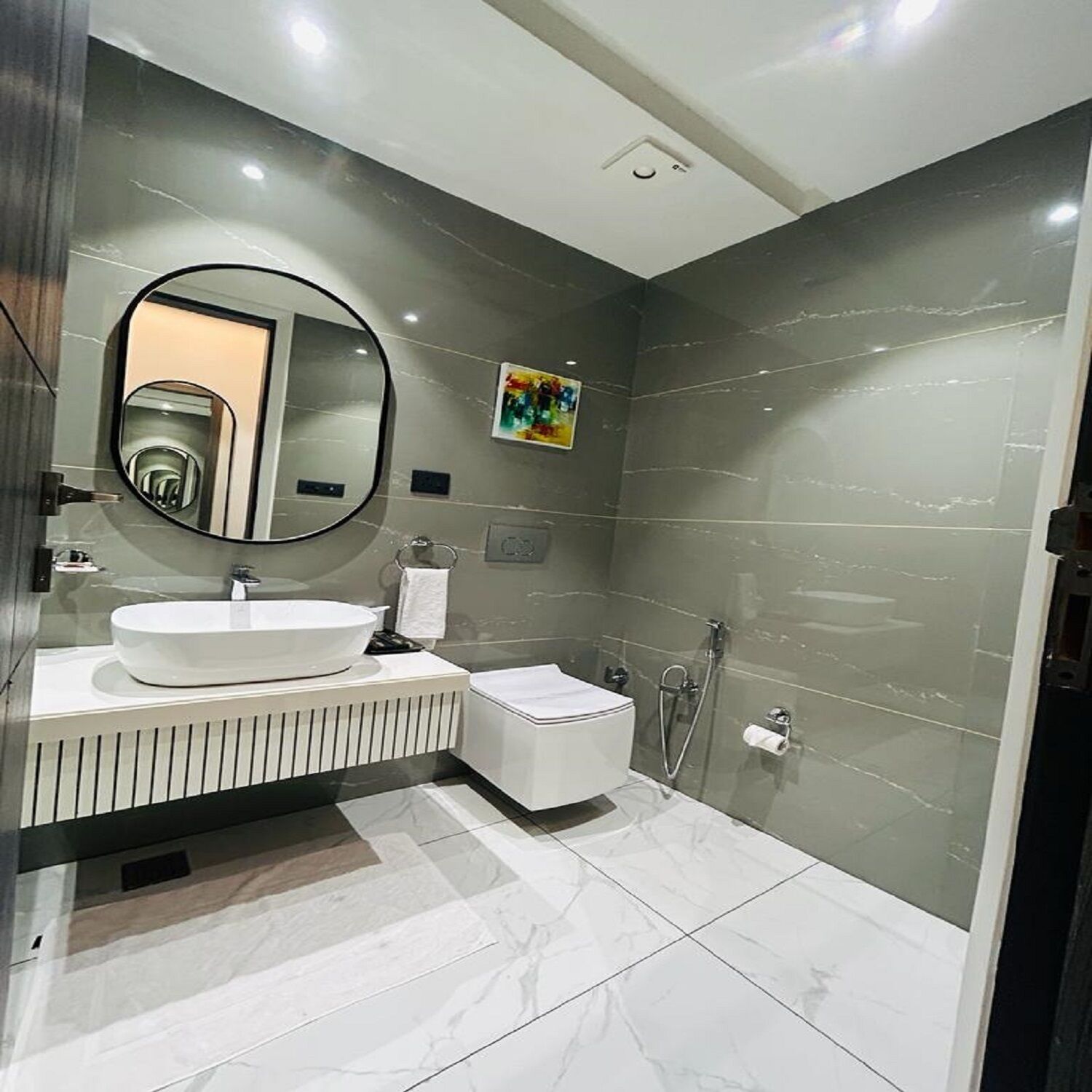 A modern bathroom with a large oval mirror, a white sink, a toilet, and a shower area.