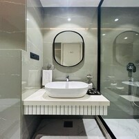 A modern bathroom with a large oval sink, a round mirror, and a glass shower enclosure.
