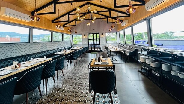 Ein Restaurant mit hoher Decke, Holzbalken und einer zentralen Sitzgruppe mit Tischen und Stühlen.