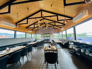 Un restaurante con techo alto, vigas de madera y una zona central con mesas y sillas.