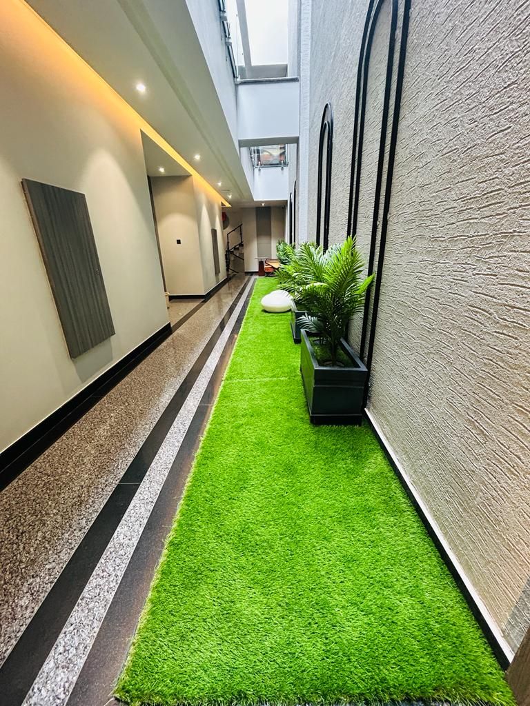 A narrow hallway with artificial green turf, black and white striped flooring, and black planters with green plants.