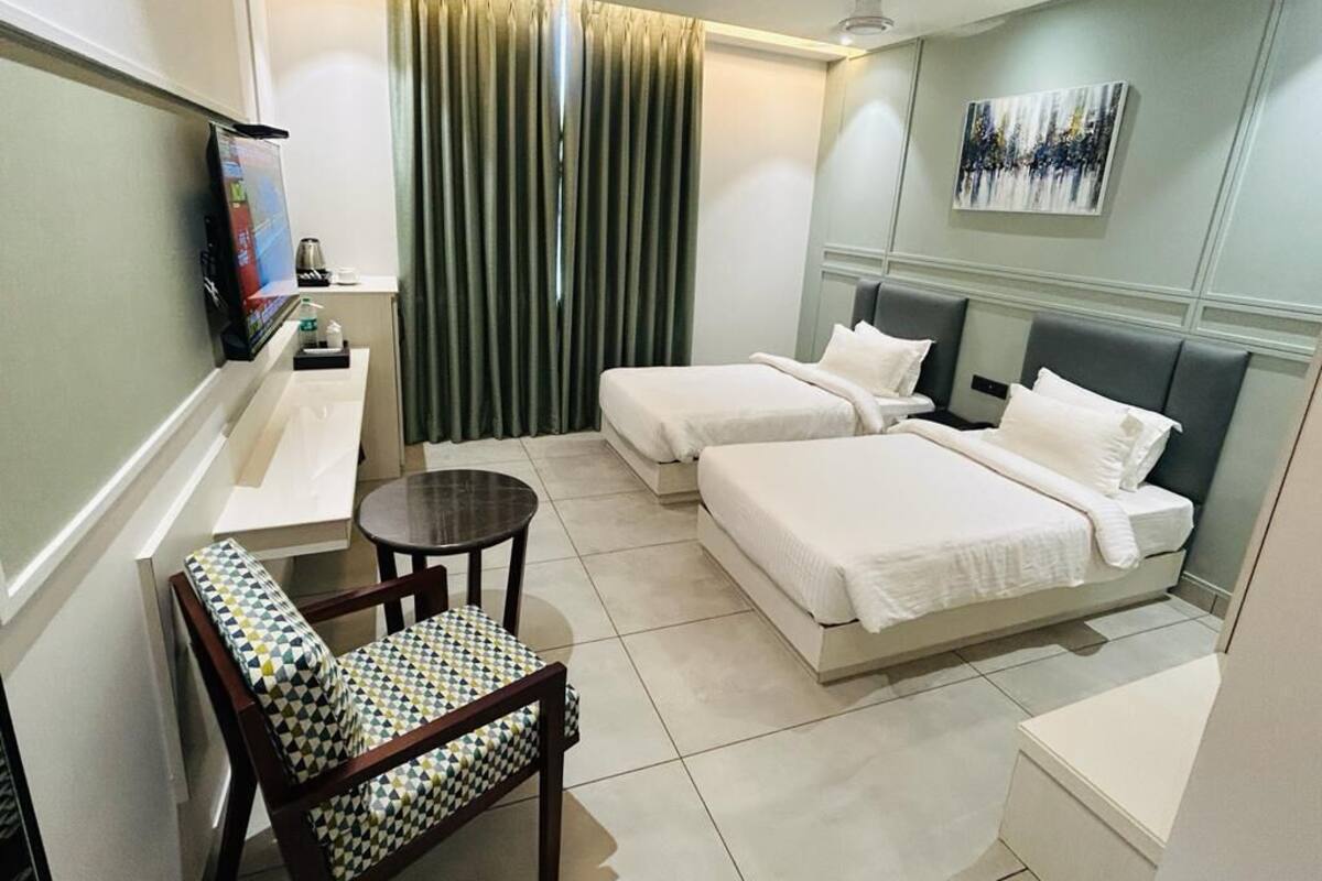Une chambre d’hôtel avec deux lits, une petite table, une chaise, un téléviseur et un tableau au mur.