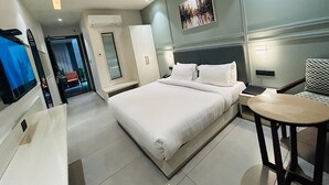 Ein modernes Hotelzimmer mit einem großen Bett, einem Schreibtisch, einem Sessel und einem Fernseher.