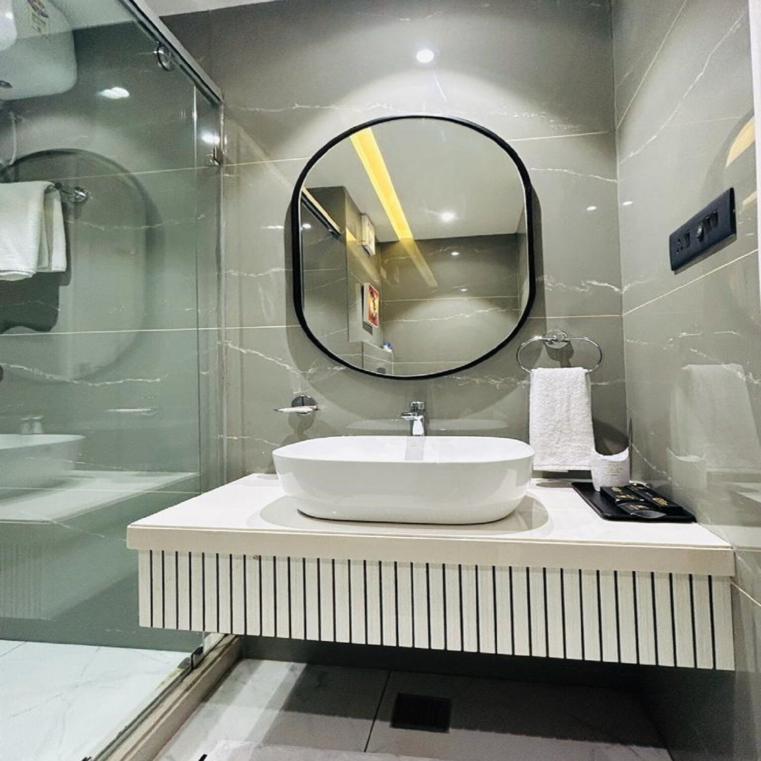 A modern bathroom with a white sink, a round mirror, and a glass shower enclosure.