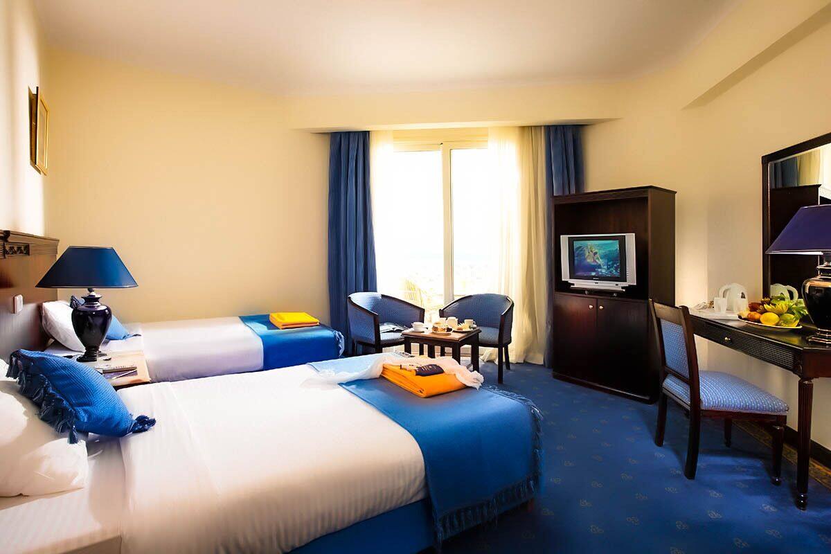 A hotel room with a large bed, a desk with a computer, a chair, and a television.