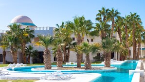 A pool area with palm trees, lounge chairs, and a building with a dome. - White Valley Palace  (Hurghada)