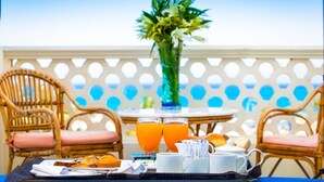 A breakfast setup with orange juice, pastries, and a tray of food on a table with wicker chairs and a white fence in the background. - White Valley Palace  (Hurghada)