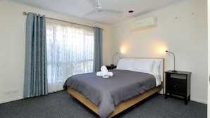 A neatly arranged bedroom with a bed, a bedside table, a lamp, and a ceiling fan. - Unit 35 Lakeview Park Bargara (Bargara)