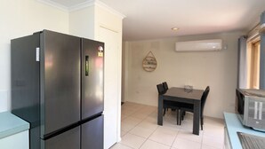 A compact kitchen with a black refrigerator, a dining table with four chairs, and a microwave. - Unit 35 Lakeview Park Bargara (Bargara)