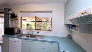 A compact kitchen with a sink, a microwave, and a window with a view of a garden. - Unit 35 Lakeview Park Bargara (Bargara)